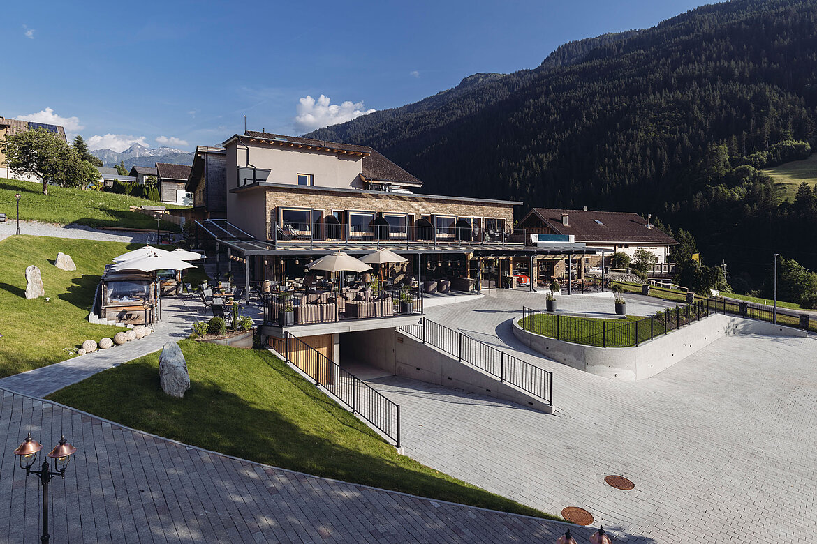 Hotelanlage des Genusshotel Vermala im Montafon mit Terrasse, Garten und alpiner Bergkulisse.