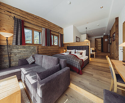 Wohn- und Schlafbereich der Suite Alpenrose im Genusshotel Vermala mit Sofa, Doppelbett, Natursteinwand und Holzinterieur.