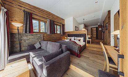 Wohn- und Schlafbereich der Suite Alpenrose im Genusshotel Vermala mit Sofa, Doppelbett, Natursteinwand und Holzinterieur.
