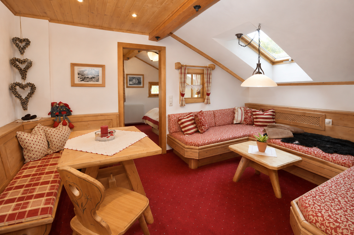 Gemütlicher Wohnbereich der Ferienwohnung Vallüla mit Eckbank, Sofa, Couchtisch, Dachfenster und Holzelementen.