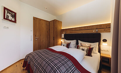 Doppelbett in der Familiensuite Edelweiß im Genusshotel Vermala mit Holzwand, gepolstertem Kopfteil und alpiner Ausstattung.