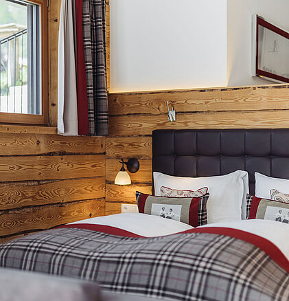 Schlafbereich der Suite Alpenrose im Genusshotel Vermala mit Doppelbett, Holzwand, Naturstein und gemütlicher Ausstattung.