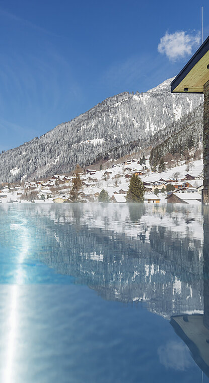 Outdoor Sky Pool im Winter im Genusshotel Vermala im Montafon mit warmem Wasser und Blick auf verschneite Berge.