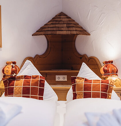 Detailaufnahme des Doppelbetts im Zimmer Heimatliebe Komfort im Genusshotel Vermala mit alpinem Holzdesign und Karokissen.
