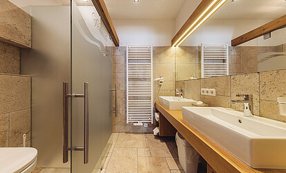 Badezimmer der Suite Alpenrose im Genusshotel Vermala mit Dusche, Doppelwaschbecken, WC und moderner heller Ausstattung.