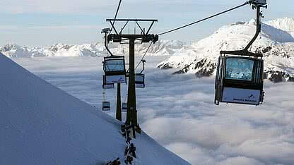 Historische Aufnahme der alten Valiserabahn im Montafon mit Gondeln über verschneiter Berglandschaft und Wolkenmeer.