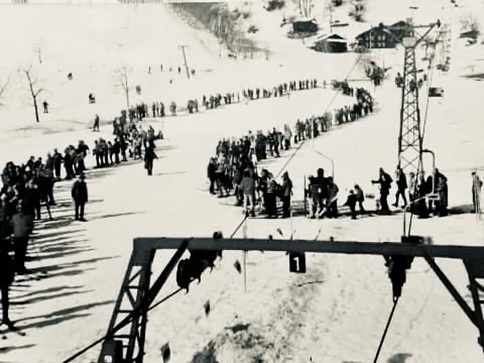 Historische Aufnahme des Versettla Sessellifts im Montafon mit langer Warteschlange, Skifahrern und verschneiter Piste.