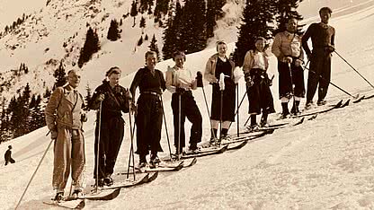 Historische Aufnahme von Skifahrern im Montafon mit Holzski, Skistöcken und verschneiter alpiner Berglandschaft.