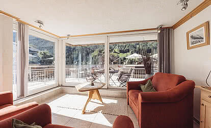 Wohnbereich der Familiensuite Heimatliebe im Genusshotel Vermala mit Sofa, Panoramafenstern, Terrasse und Blick auf St. Gallenkirch.