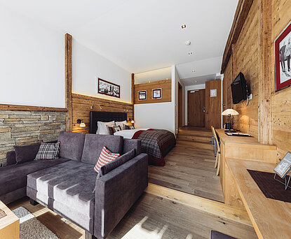 Suite Brunella im Genusshotel Vermala mit Wohnbereich, Sofa, Doppelbett, Schreibtisch und Natursteinwand.