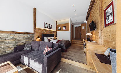 Suite Brunella im Genusshotel Vermala mit Wohnbereich, Sofa, Doppelbett, Schreibtisch und Natursteinwand.