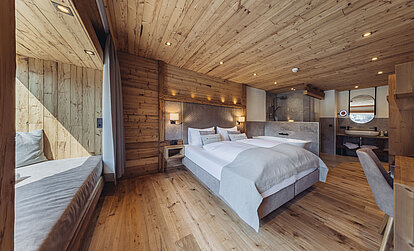 Zimmer Heimatblick im Genusshotel Vermala mit Doppelbett, offenem Wohn- und Badbereich, Spiegel und Montafoner Holzinterieur.