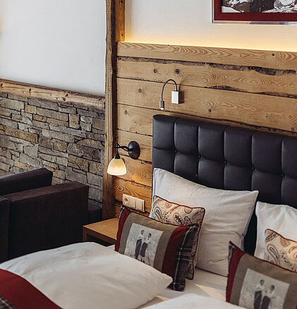 Schlafdetail der Suite Brunella im Genusshotel Vermala mit Doppelbett, Holzwand, Naturstein und dekorativen Kissen.