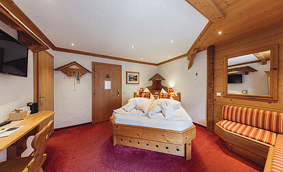 Zimmer Heimatliebe Komfort im Genusshotel Vermala im Montafon mit Doppelbett, Sofa, Schreibtisch und alpinem Holzdesign.