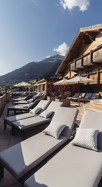 Sonnenliegen im Weitblick SPA des Genusshotel Vermala mit Whirlpool, Hotelgebäude und Bergblick.