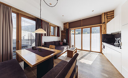 Wohn- und Essbereich der Familiensuite Edelweiß im Genusshotel Vermala mit Eckbank, Sofa, Panoramafenstern und Balkonzugang.