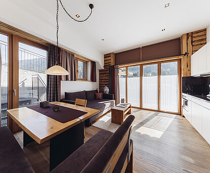 Wohn- und Essbereich der Familiensuite Edelweiß im Genusshotel Vermala mit Eckbank, Sofa, Panoramafenstern und Balkonzugang.