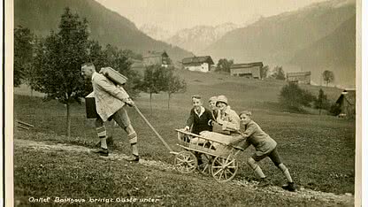 Historische Aufnahme vom Gästetransport in Sponna im Montafon mit handgezogenem Wagen und alpiner Landschaft.
