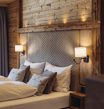 Schlafbereich im Zimmer Heimatblick des Genusshotel Vermala mit Doppelbett, Holzverkleidung, Leselampen und alpinem Design.