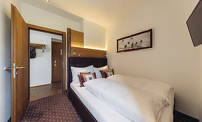 Schlafzimmer der Familiensuite Edelweiß im Genusshotel Vermala mit Doppelbett, Holzelementen und Zugang zum Badezimmer.